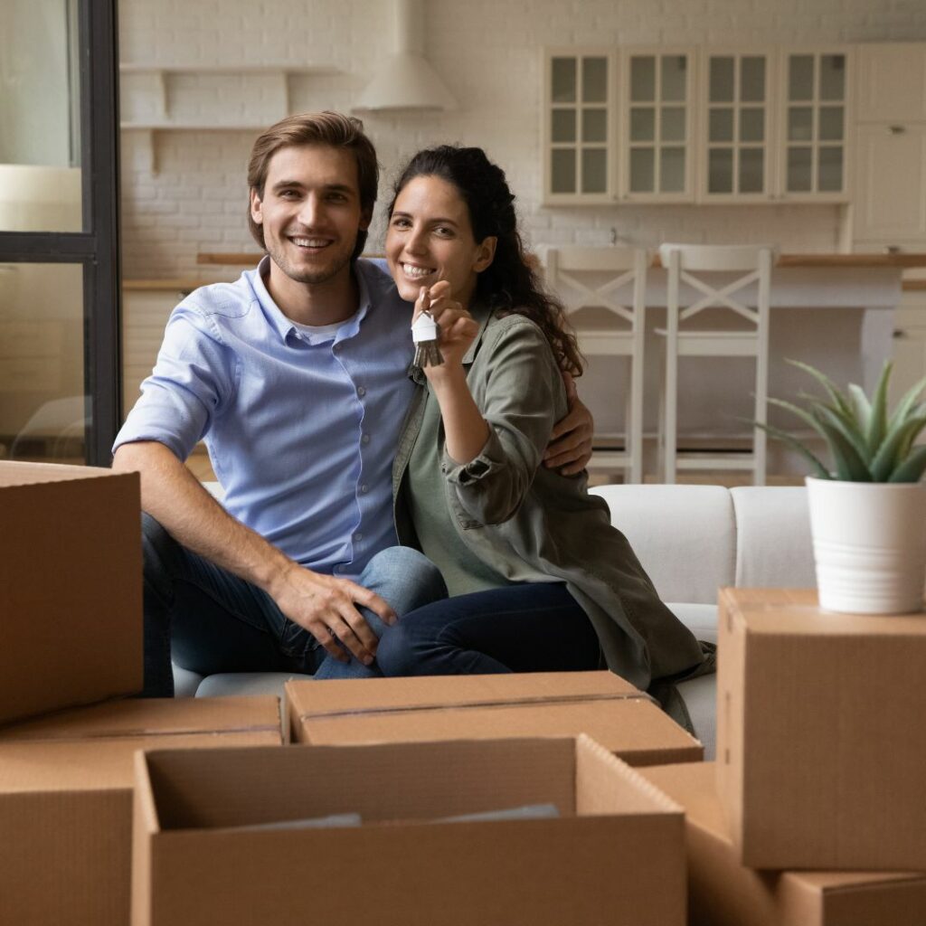 Young couple among moving boxes holding new house keys and smiling