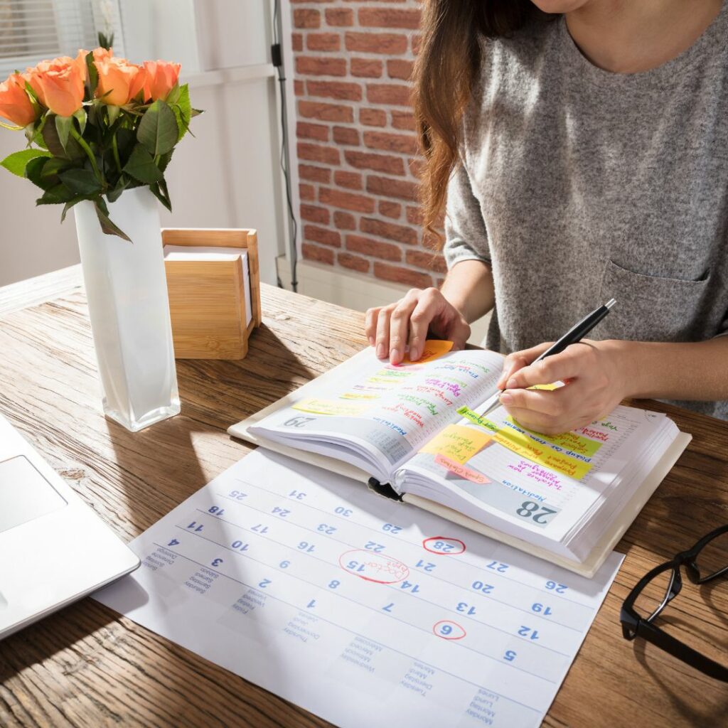 Woman writing in planner and looking at calendar while sitting at a desk