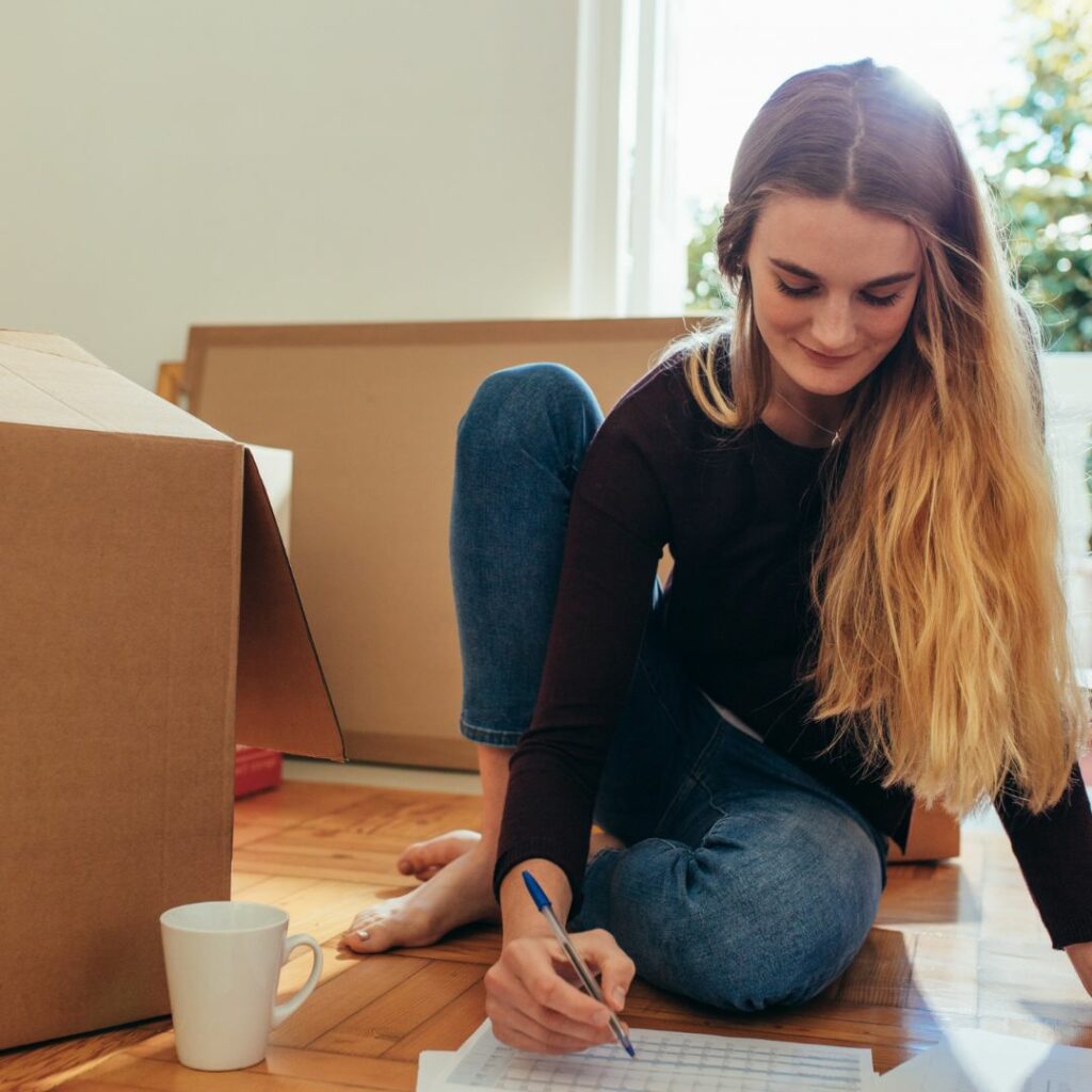 Young woman crossing items off a list, sitting among moving boxes