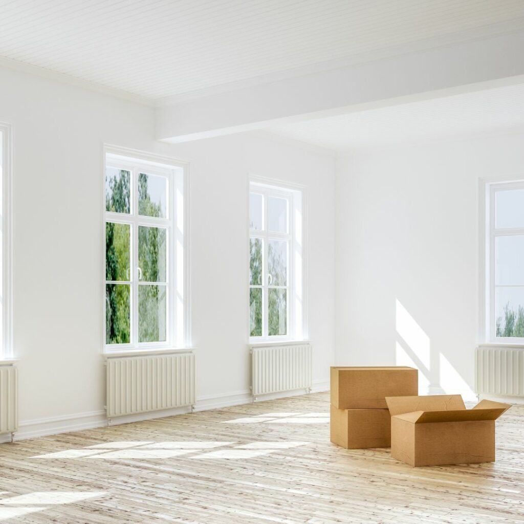 Empty room with three moving boxes and windows with radiators beneath them