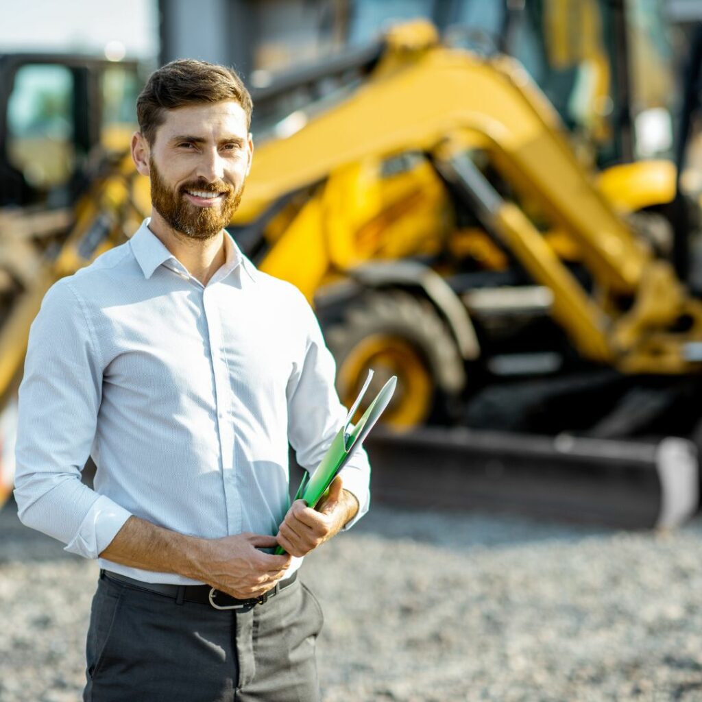 man with folder in front of heavy machinery